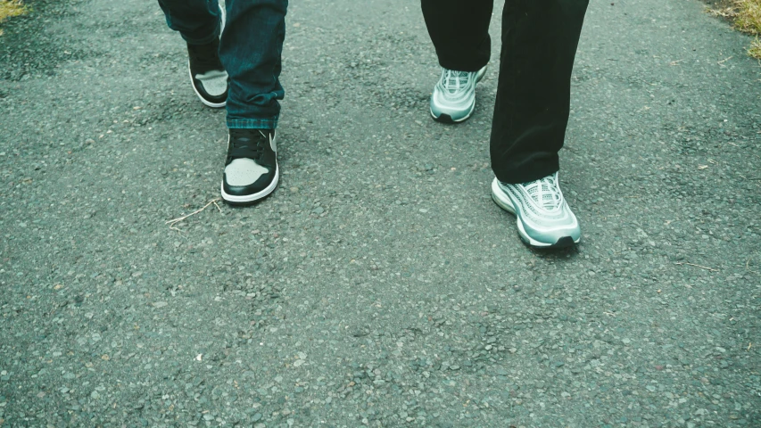 two persons walking along a paved walkway, both with white shoes