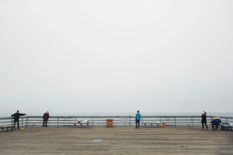 four people standing on a pier looking out over the ocean