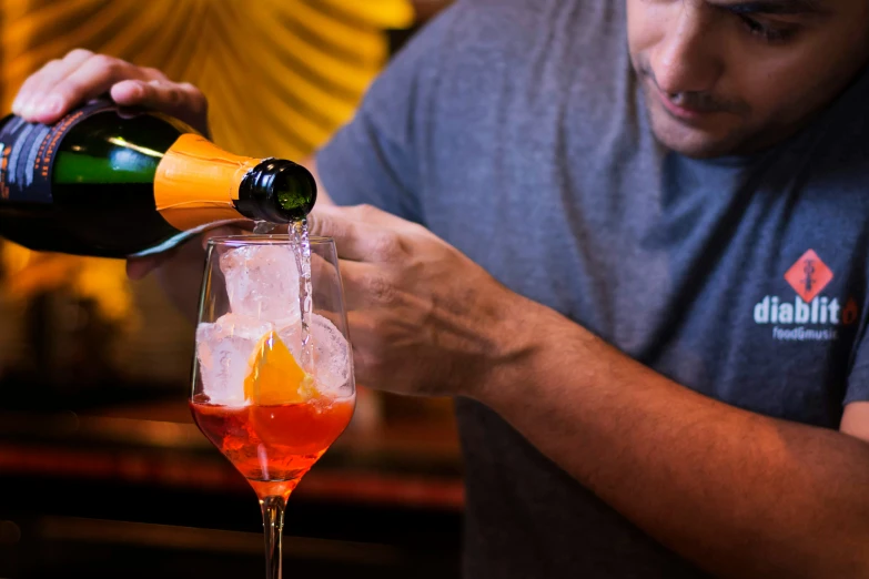 a man pouring alcohol into a cocktail with orange wedges