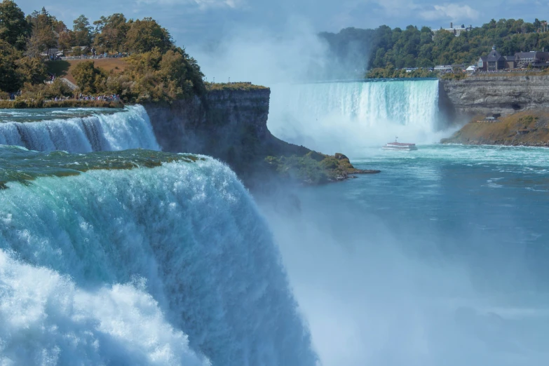 a waterfall with water splashing over it in front of the forest