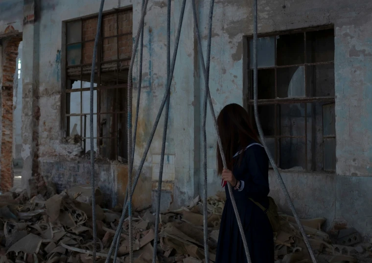 a woman walking past an abandoned building holding rope