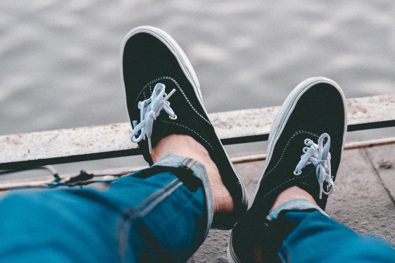 someone in vans shoes with a boat and water in the background