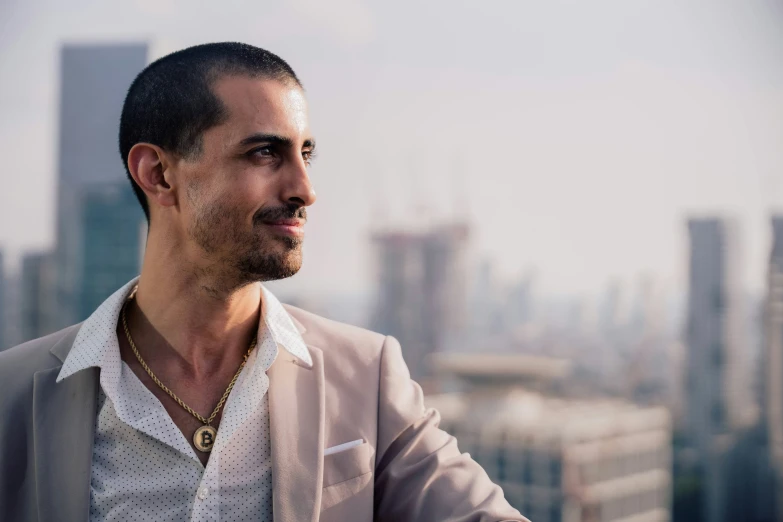 a man wearing a beige suit and gold necklace