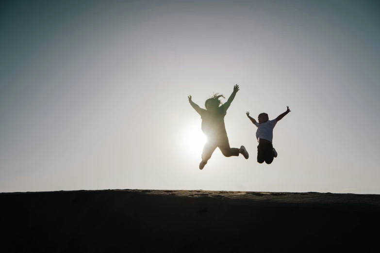 a man and woman jumping in the air on top of a hill