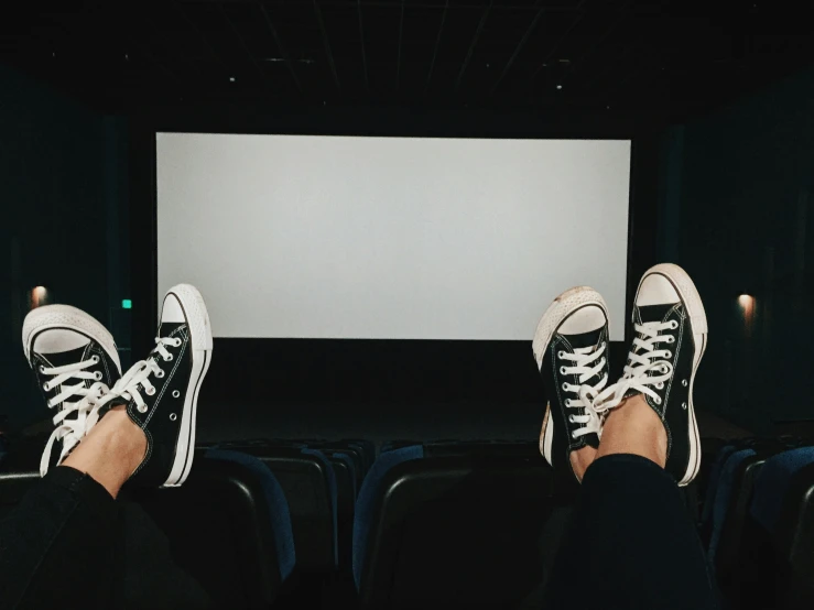 feet in black sneakers are in a darkened room with an empty screen