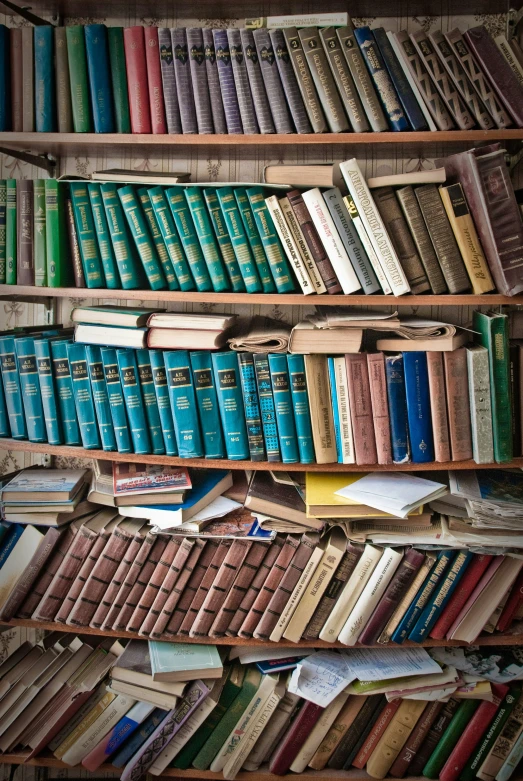 a long wooden bookshelf is filled with rows and piles