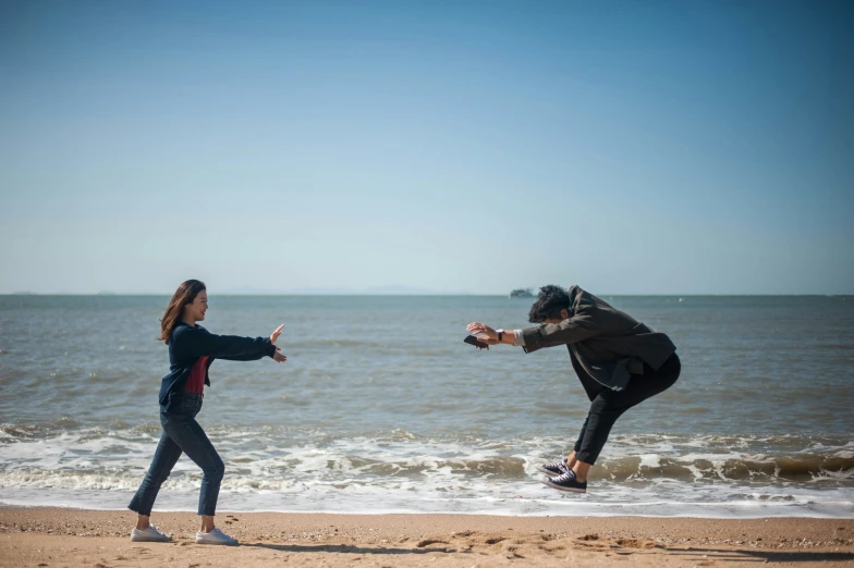 two people on a beach facing the ocean with one holding the other out