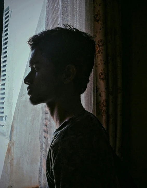 a young man looking out the window in his house