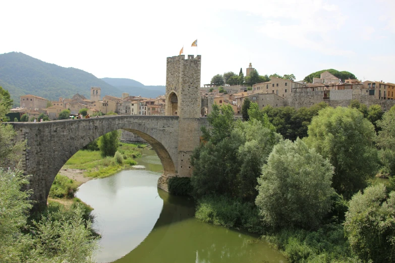 a stone bridge crosses a small river below a medieval town