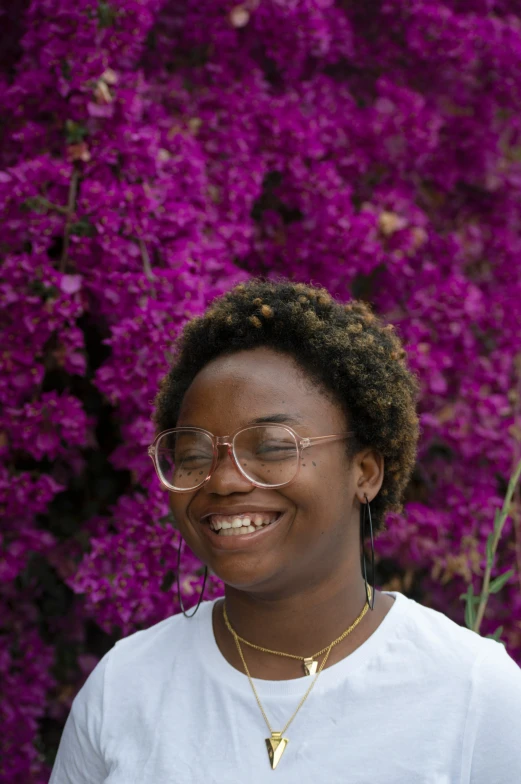 a woman wearing glasses standing in front of some pink flowers