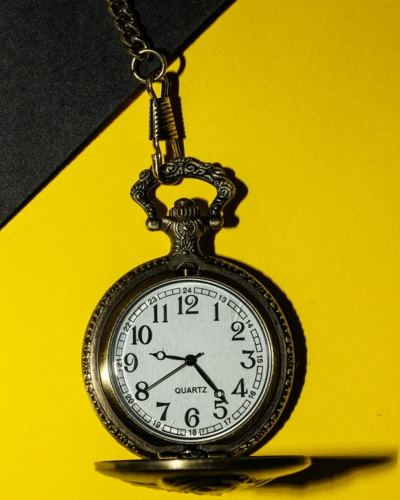 a close - up s of an old pocket watch on a chain on yellow and black striped background