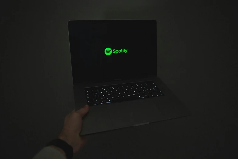 someone's hand holding a laptop with a glow logo on it