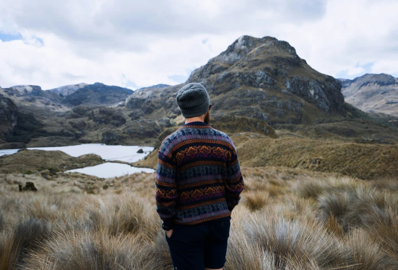 a man wearing a colorful sweater and a beret standing in a wilderness