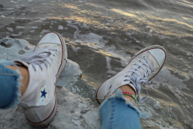 someones feet with sneakers near water with ripples