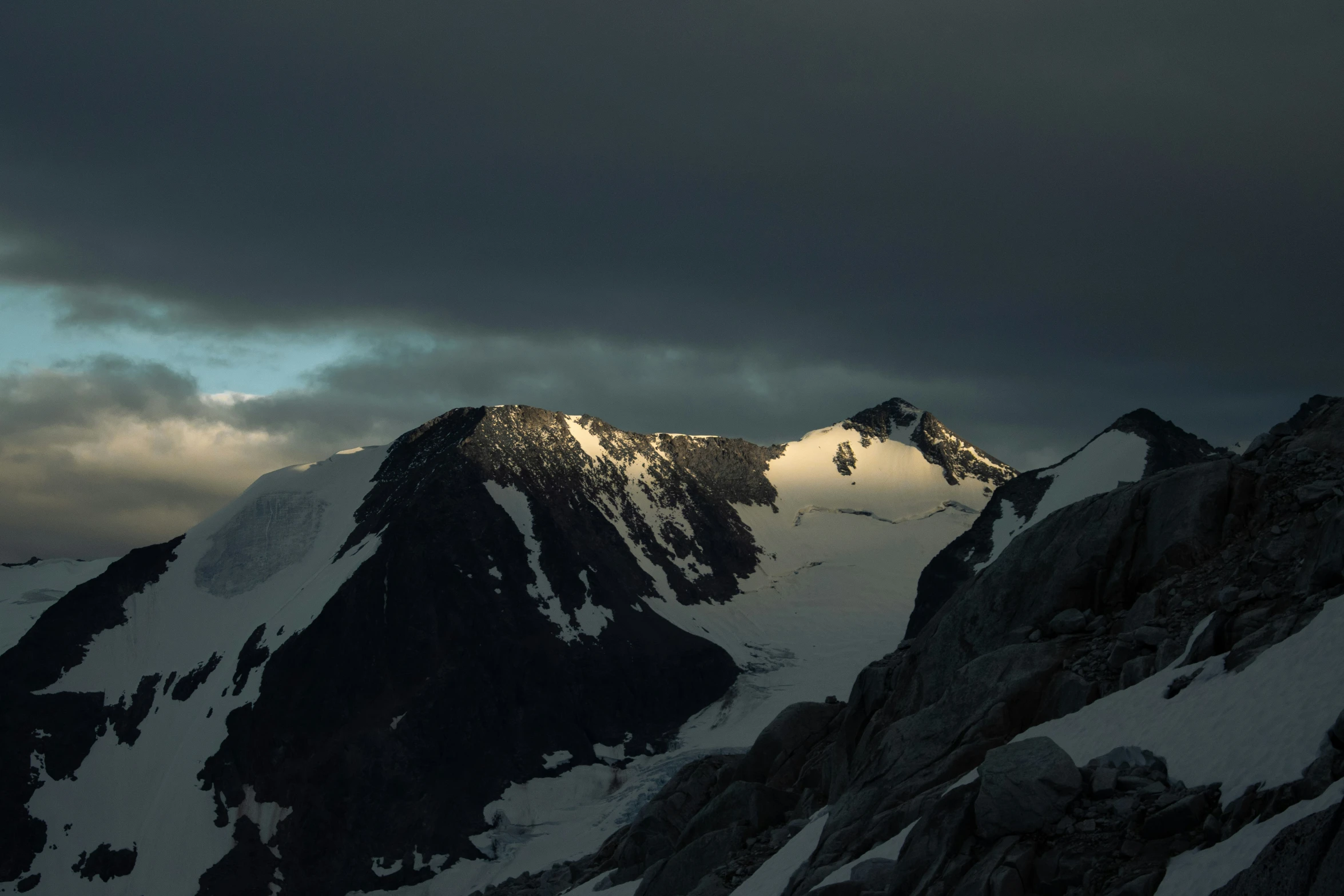 a snow covered mountain range under clouds at dusk