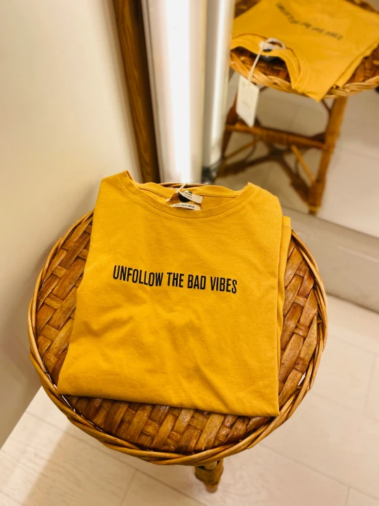 a t - shirt with the words whimfolly the bad vibes written on it sits on a wicker stool next to a mirror