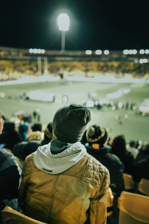 a person in a brown jacket and a white scarf is sitting in the stands