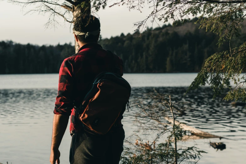 man with backpack looking over water on a lake