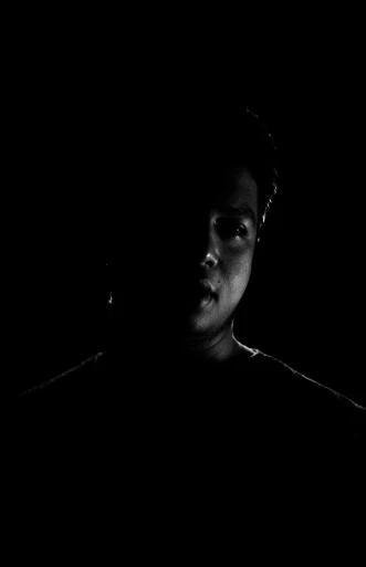 a man in dark room with black background looking at his cellphone