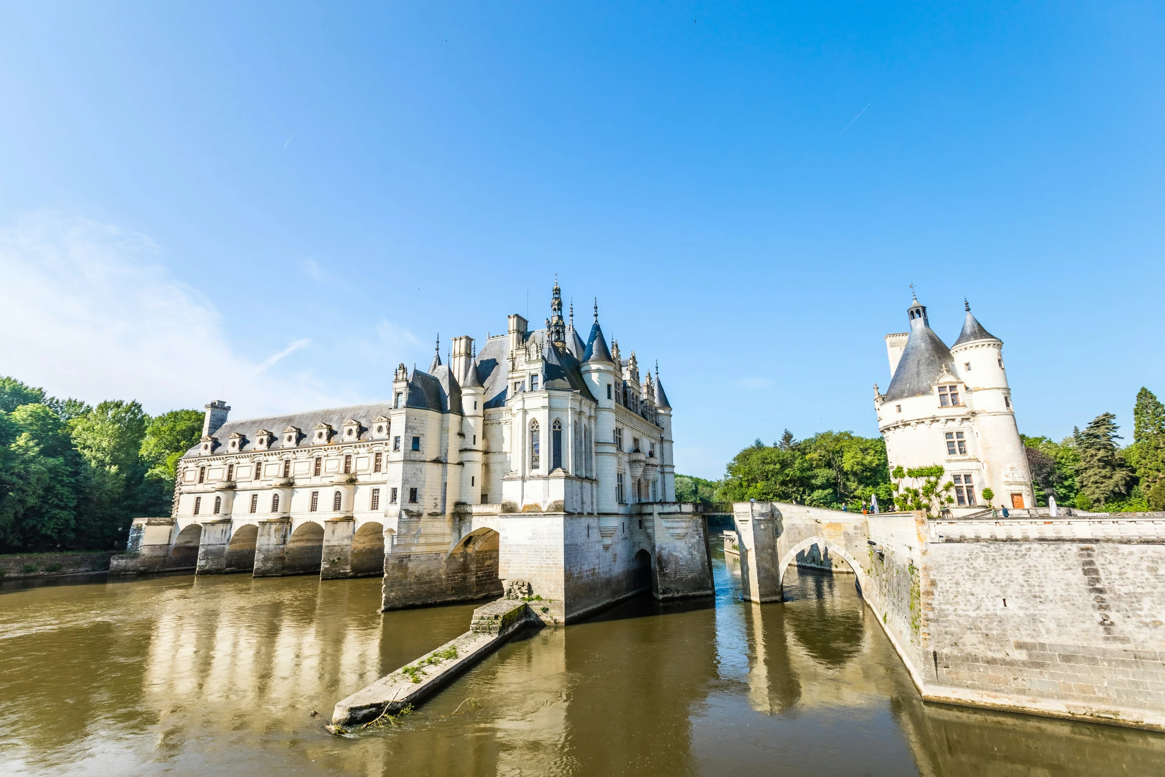 a large castle sits on a river by a bridge