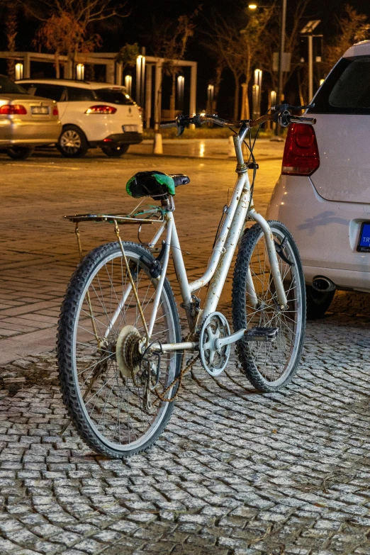 a white bike on brick pavement near parked cars