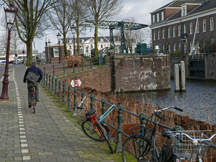 person riding bicycle on path next to canal with parked bicycles