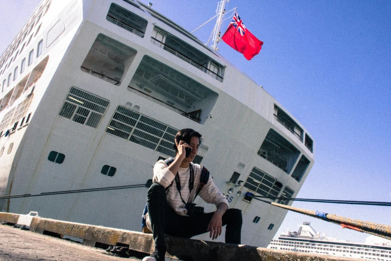 a girl sitting on the concrete beside a boat and talking on her cellphone