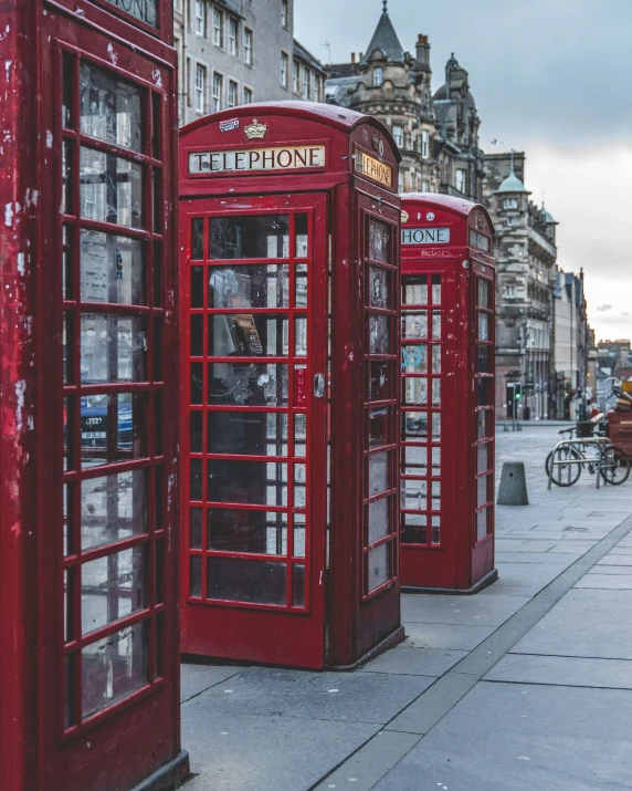 three red phone booths line the street as bicycles go by