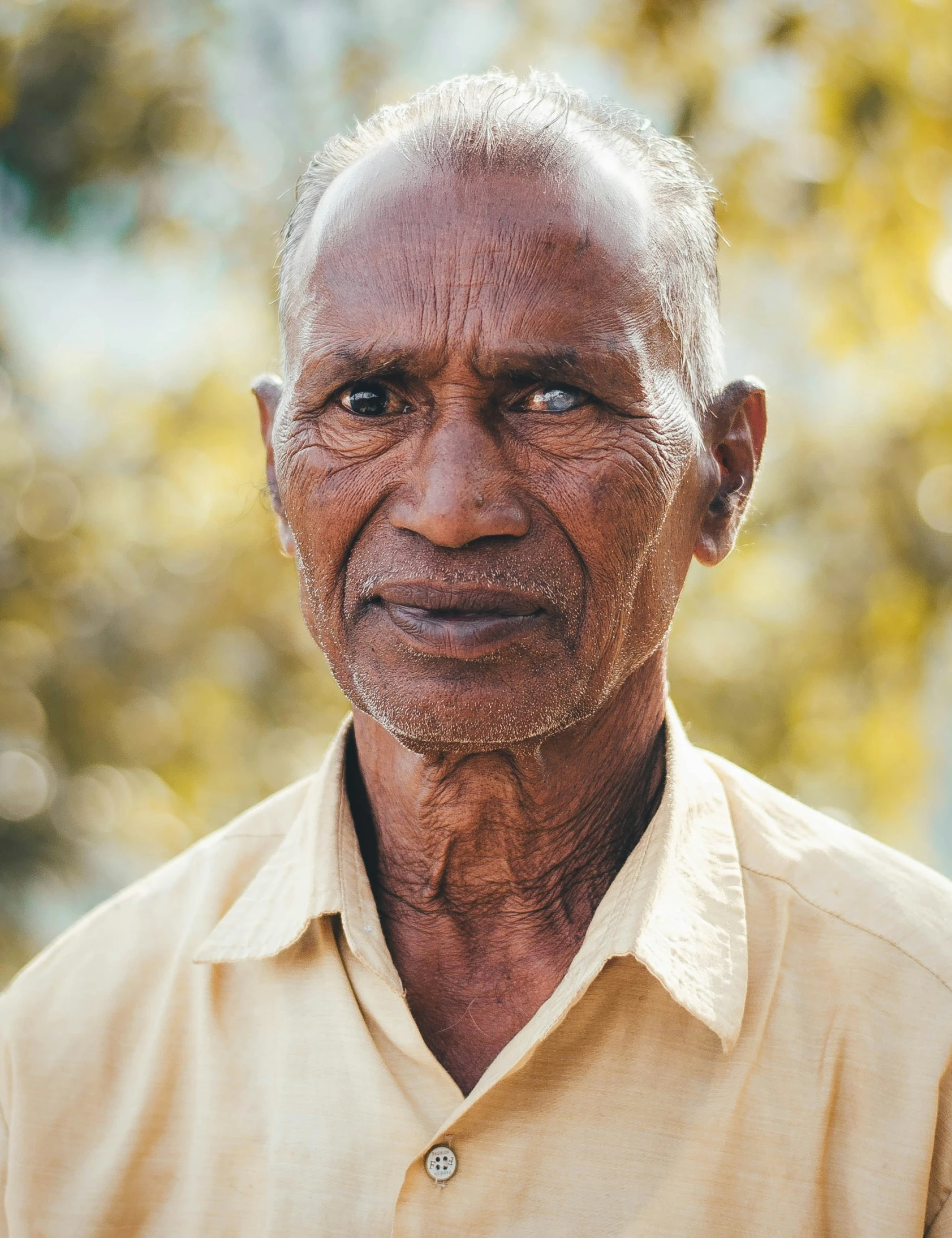 a man standing in front of some trees wearing a tan shirt