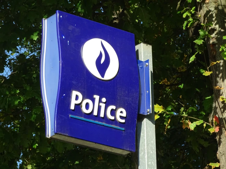 a blue police sign sitting under trees