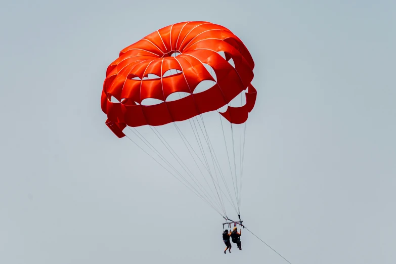 a person parasails high in the air with orange colored parachutes