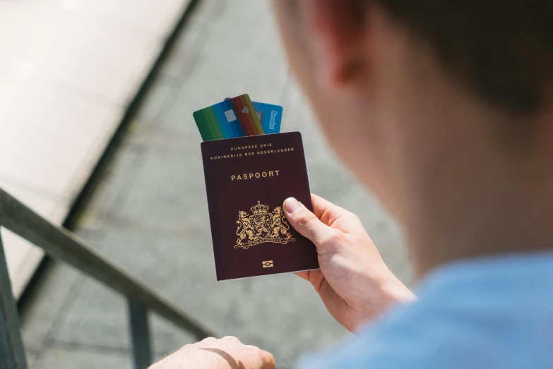 a man holding an open passport and three pens