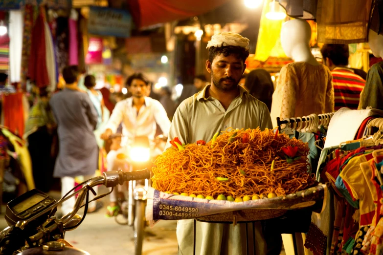 a man stands on a crowded street holding a tray full of noodles