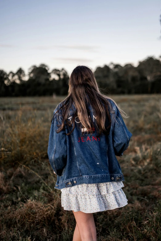 back view of woman walking in field wearing blue denim jacket