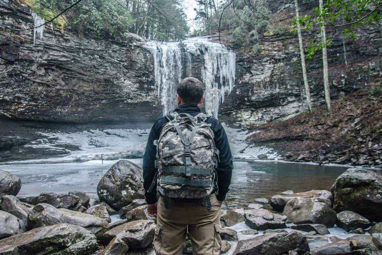 a person with a backpack standing near water falls