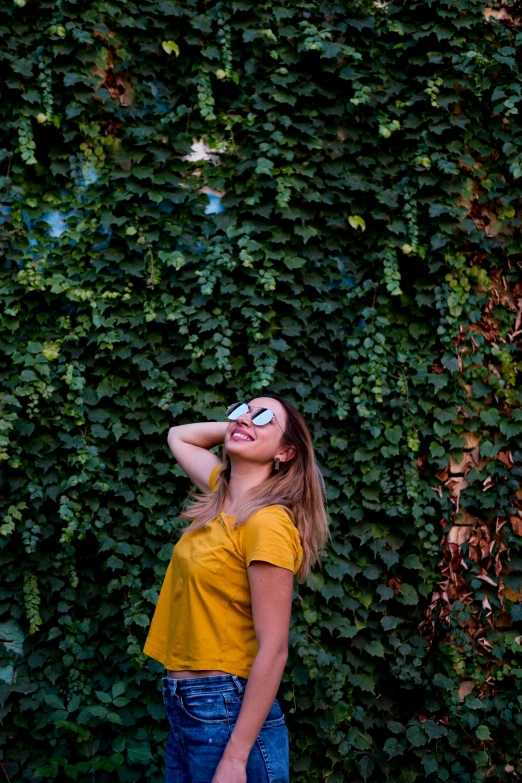 a woman in a yellow top wearing jeans stands by a green wall