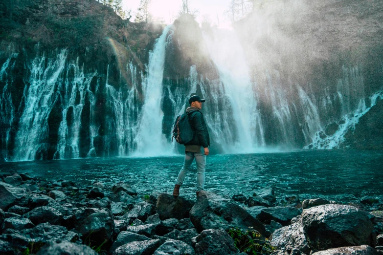 a man in a black jacket is standing by the waterfall