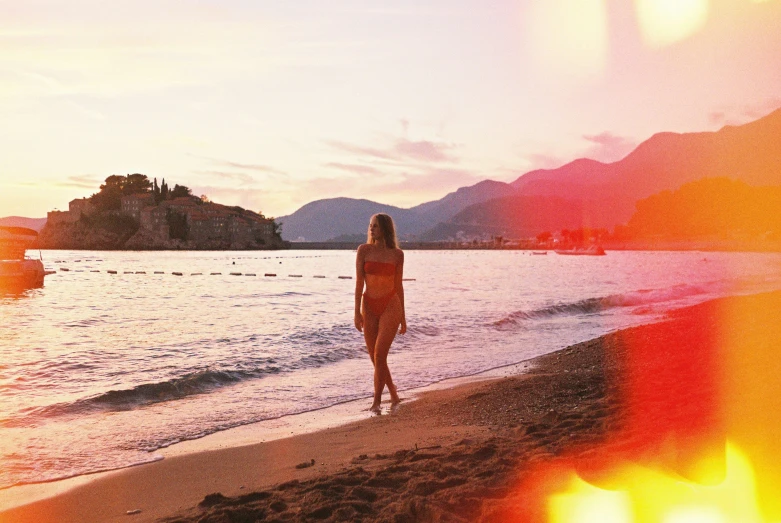 a girl is walking on the beach at sunset