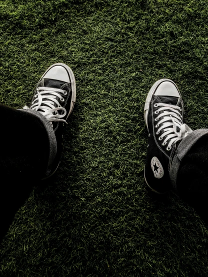two people wearing converse shoes standing on green grass