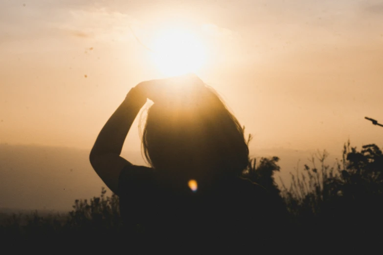 a person standing under the sun with their arm raised