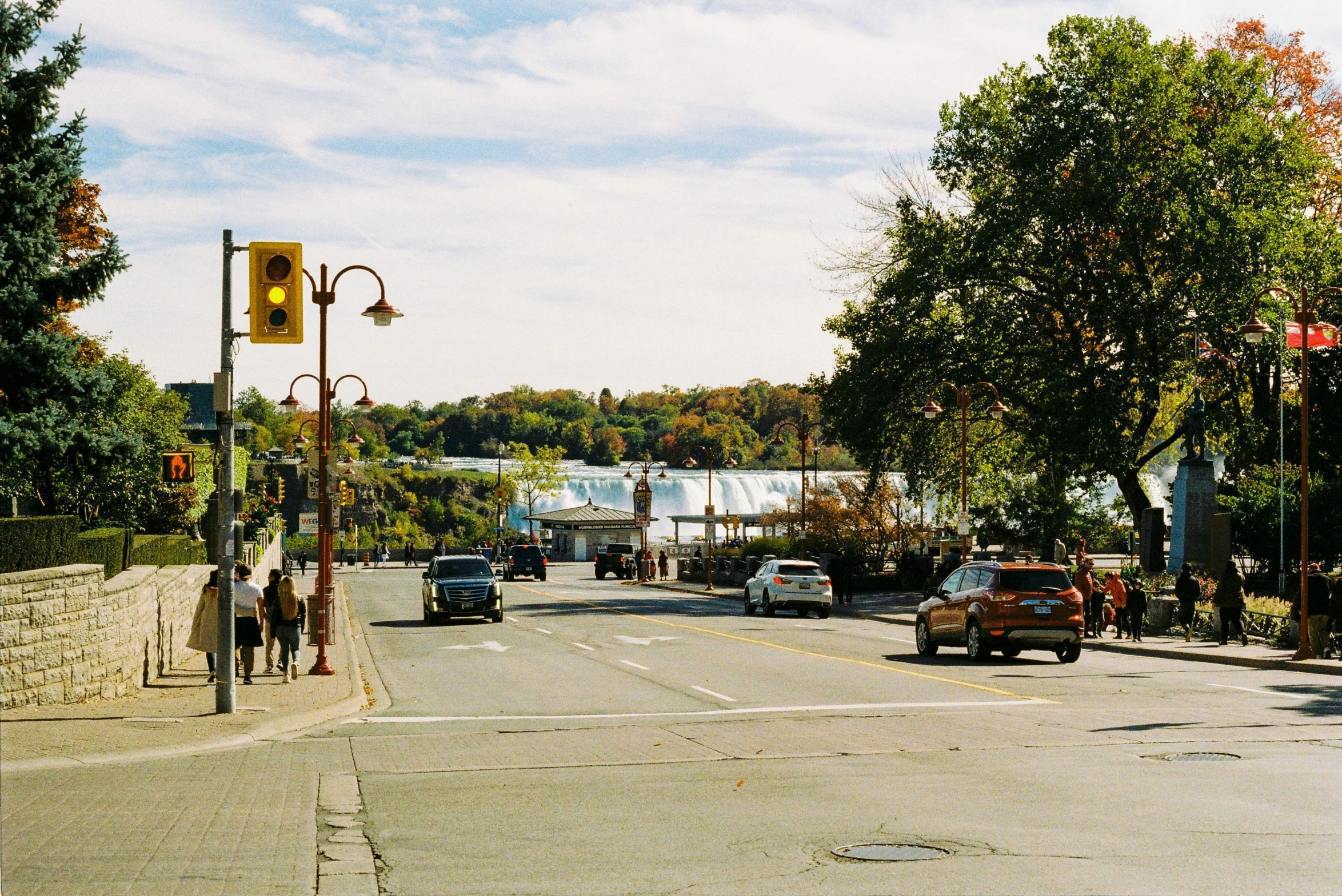 several cars driving down an urban street with fall trees