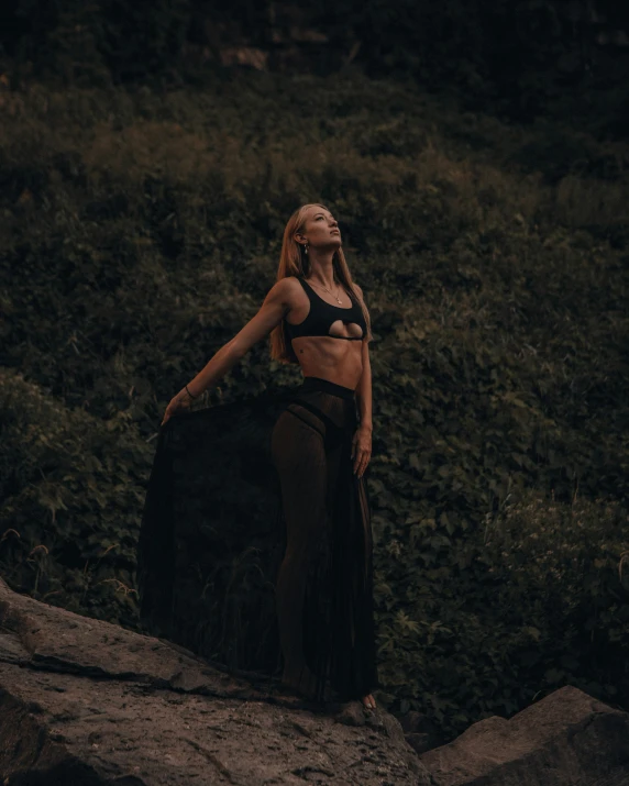 a woman in a bathing suit posing near a large rock