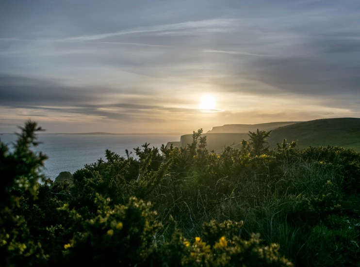 a setting sun shines over the hills on top of a cliff above the ocean