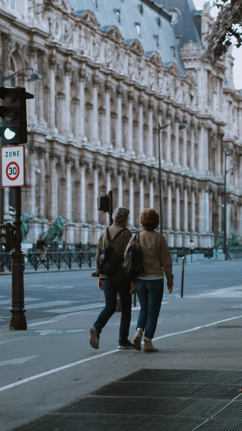 two people walking down a sidewalk past a traffic light