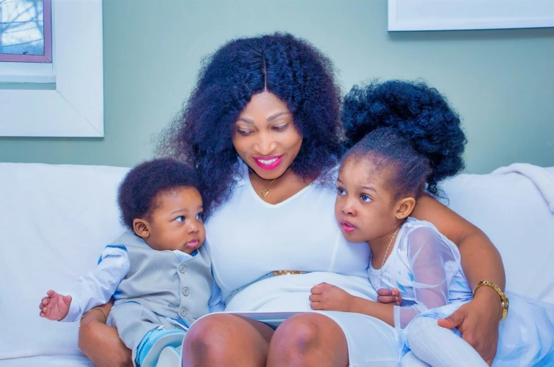 a woman sitting on top of a white couch with two children