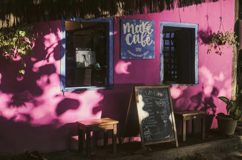 the sidewalk outside a pink restaurant has a menu and some wooden chairs