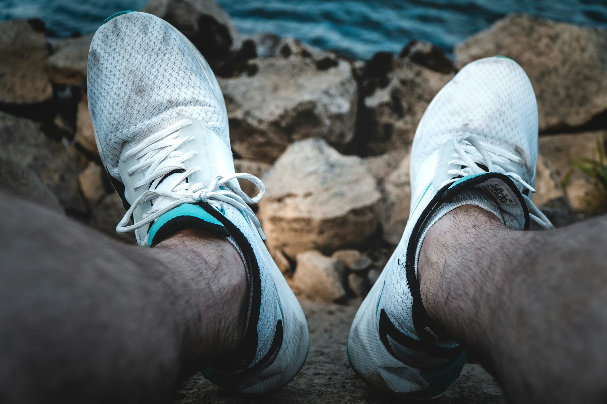 a pair of legs in sneakers with rocks in the background