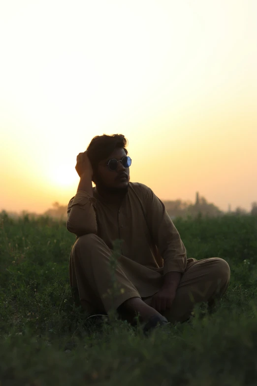 a man is sitting in the grass while talking on a cell phone