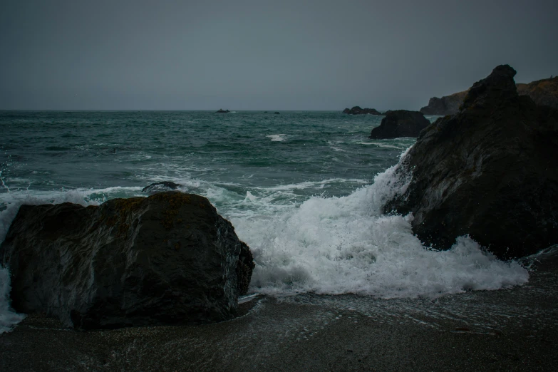 a rocky beach has a white wave coming in