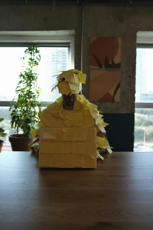 a person sitting at a wooden table with large paper wrapped around his body